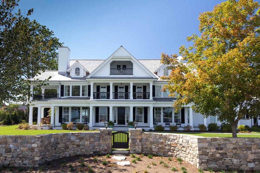 White colonial exterior house painting with black shutters and stone wall.